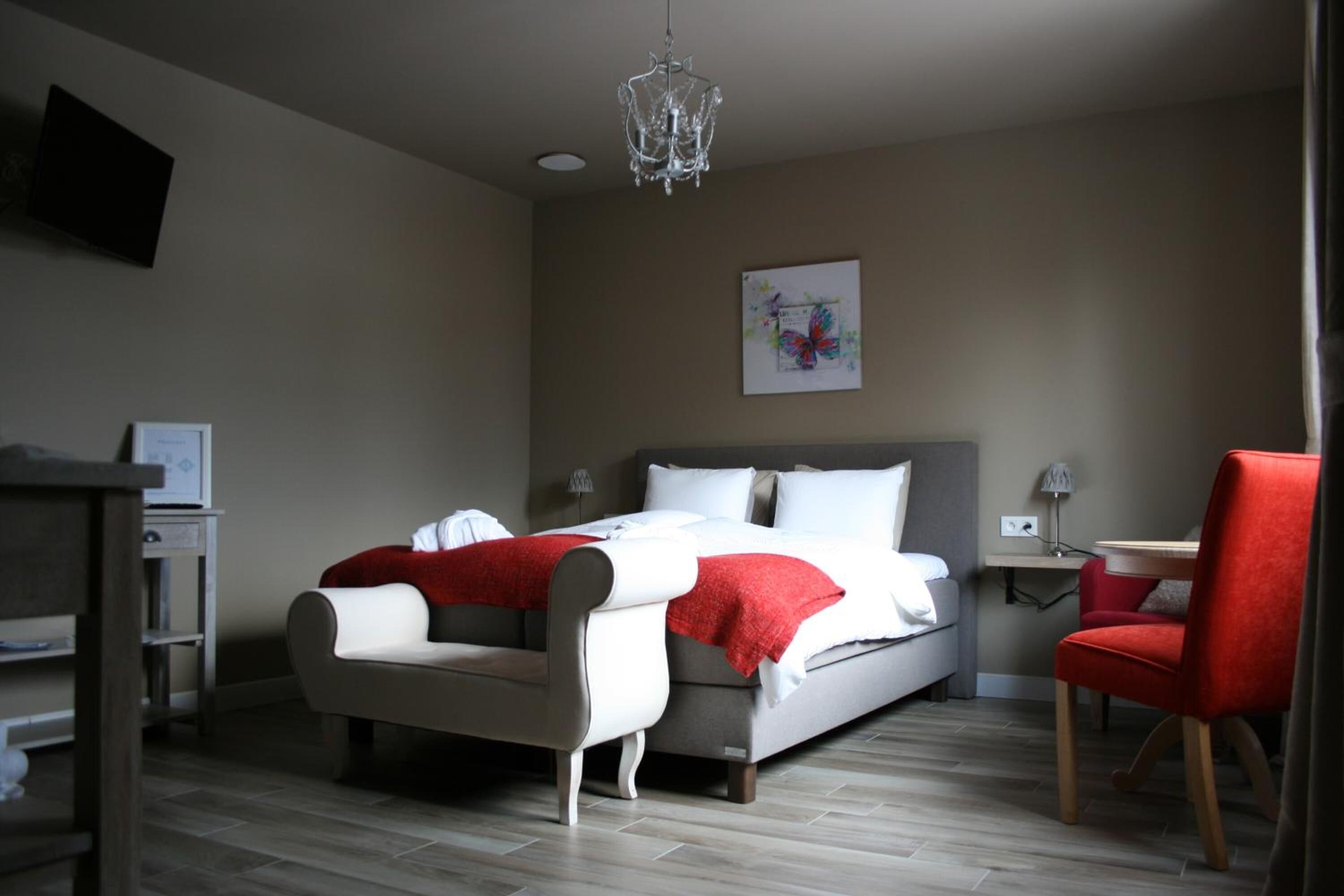 A bedroom with a bed, a red chair, a desk, and a chandelier.