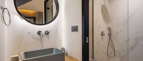 A bathroom with a marble sink, a round mirror, and a shower with a handheld showerhead.