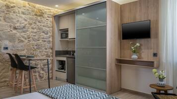 A compact room with a kitchenette, a dining area with chairs, a bed, and a TV mounted on the wall.