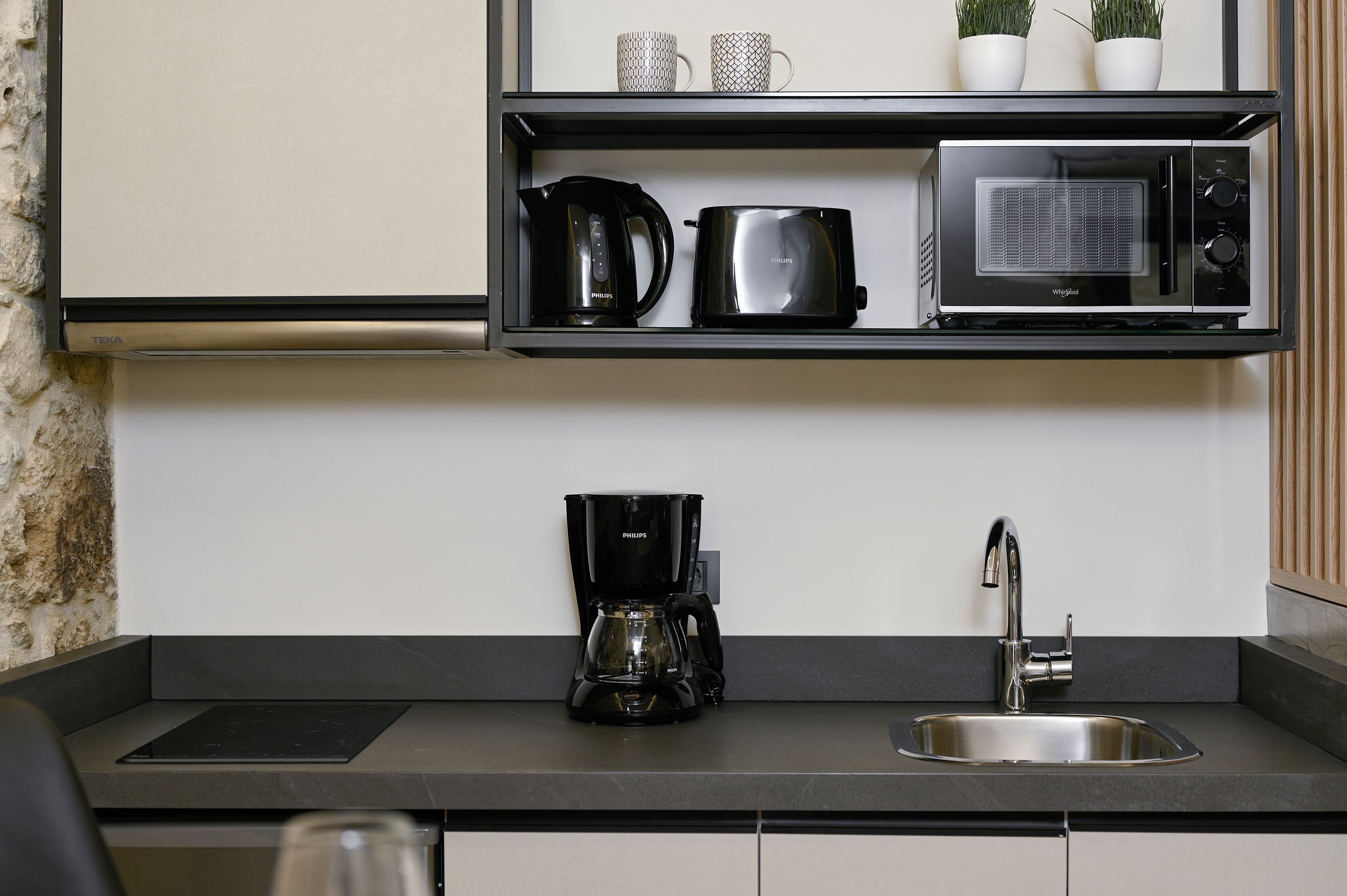 Una cocina moderna con encimera negra, cafetera, microondas y lavamanos.