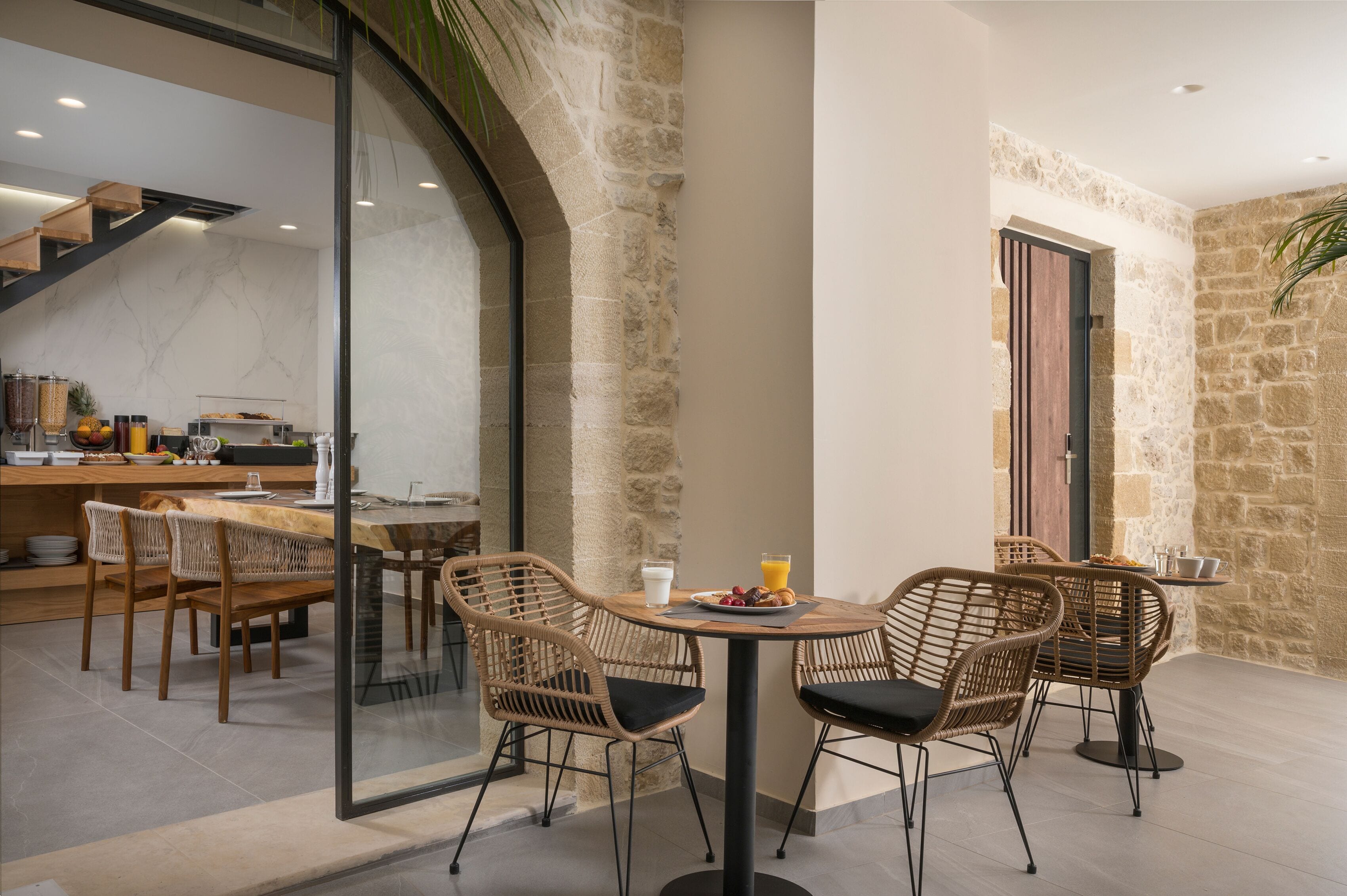 A dining area with wicker chairs and a round table, a breakfast bar with various food items, and a stone wall.