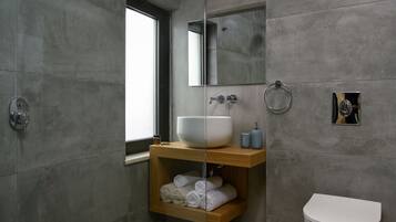Un bagno moderno con un ampio lavandino bianco, uno scaffale in legno con asciugamani, un WC e uno specchio.