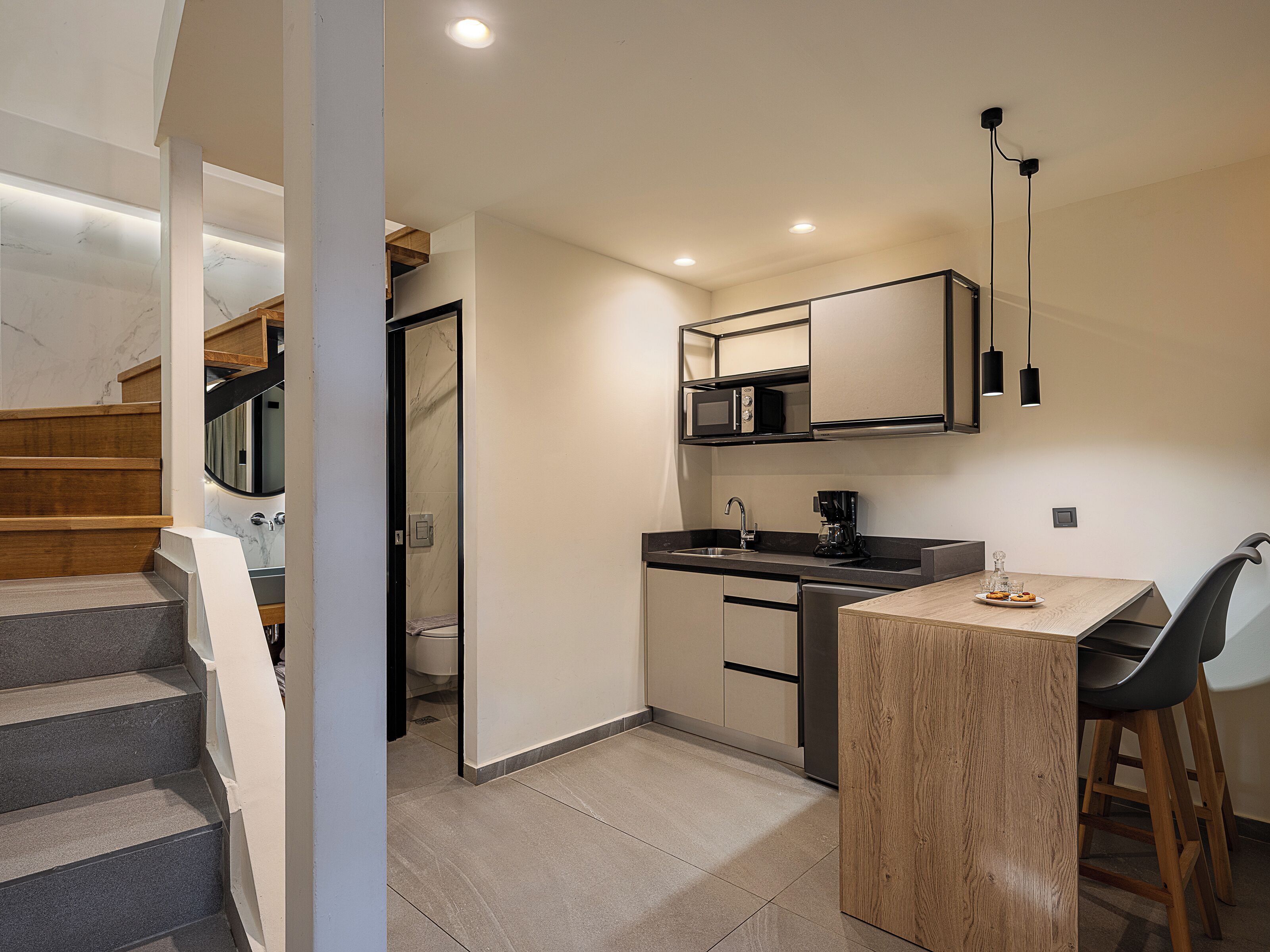 A modern kitchen with a wooden staircase, a dining area with a bar stool, and a built-in microwave.