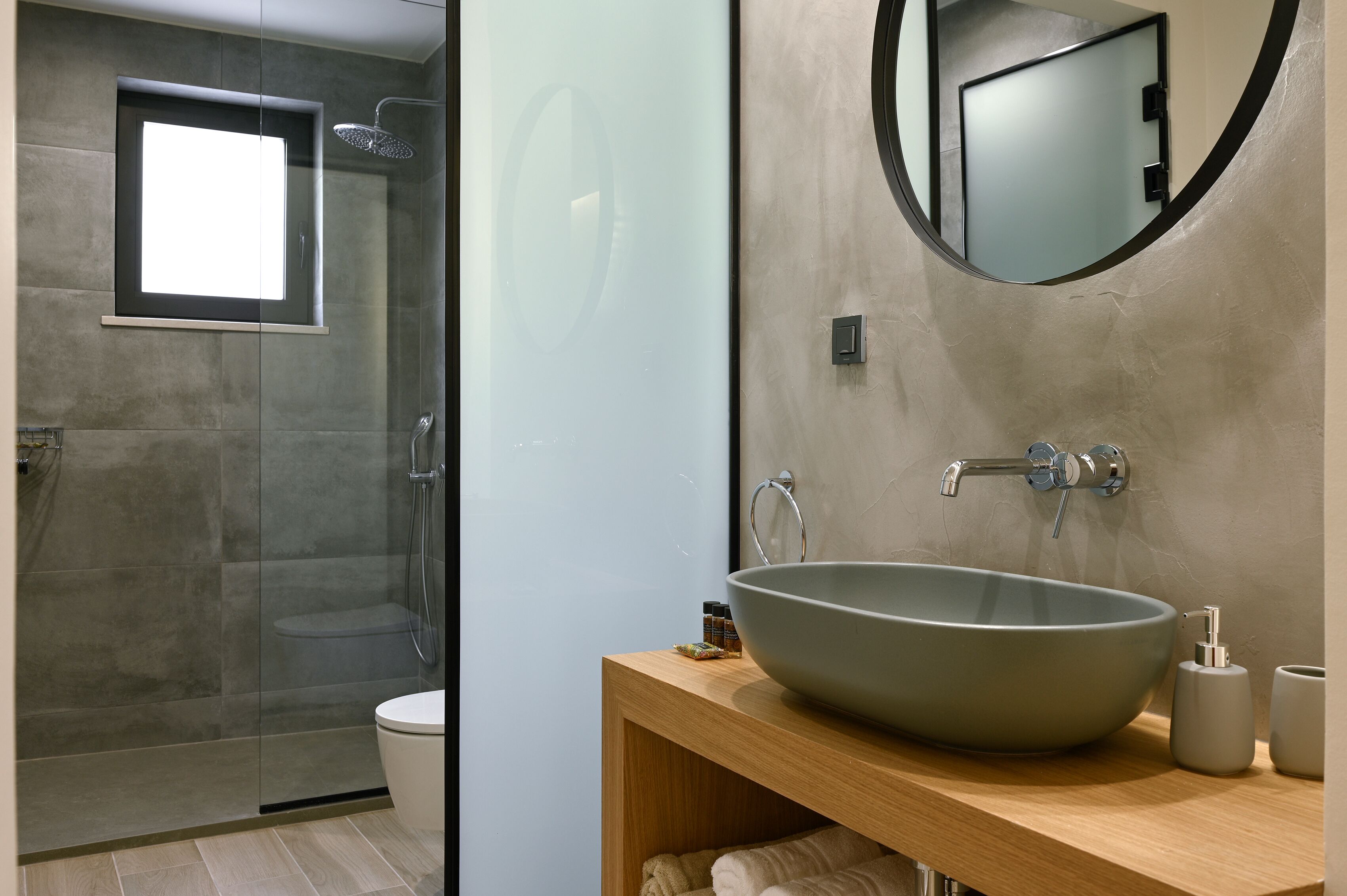 A modern bathroom with a glass shower enclosure, a large vessel sink, and a wooden vanity.