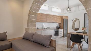 Una sala moderna con un sofá, un comedor con mesa y sillas, y una cocina con armarios de madera y un refrigerador.