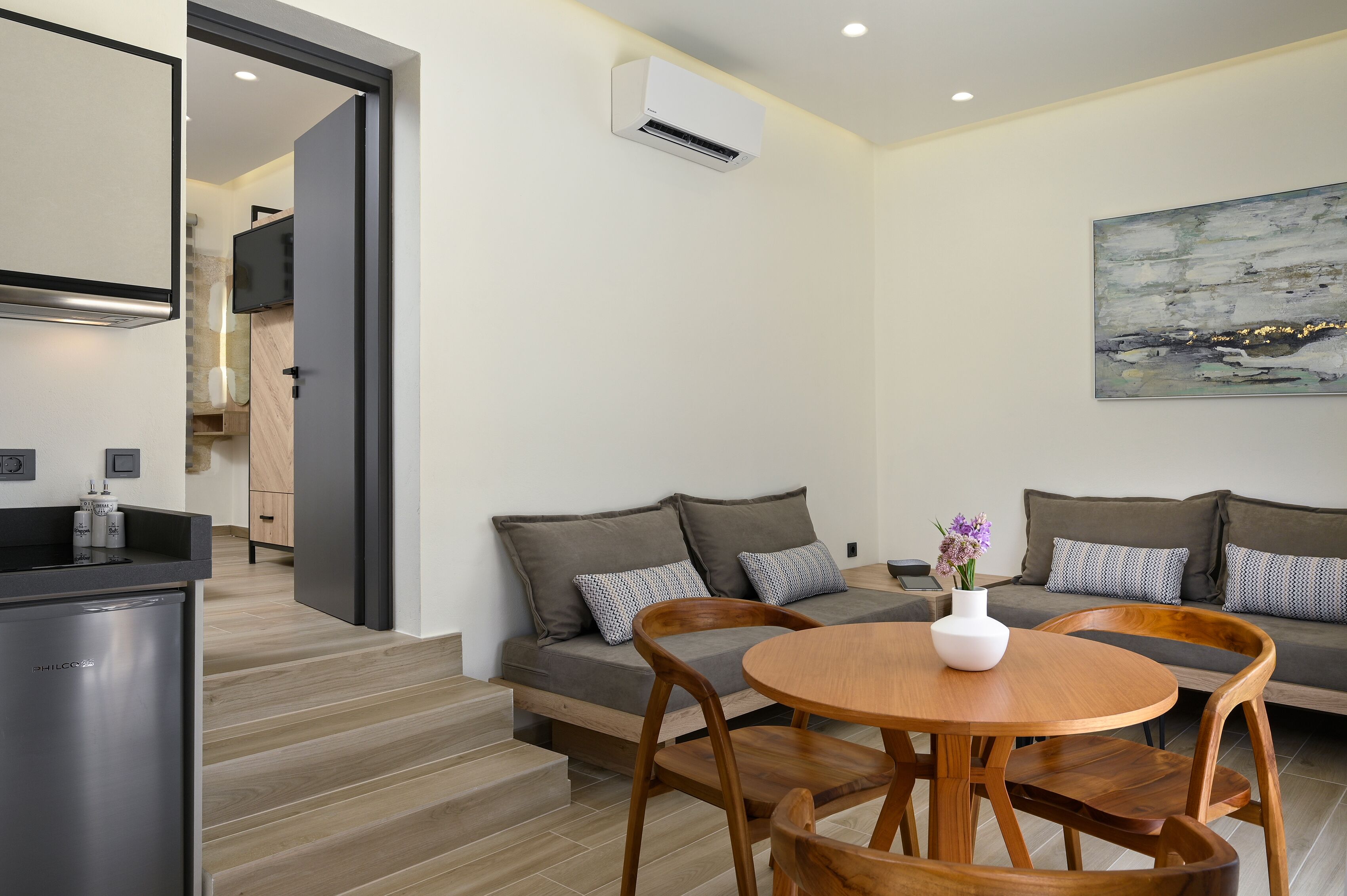 A modern living room with a sofa, a dining table, and a kitchen area with a refrigerator.