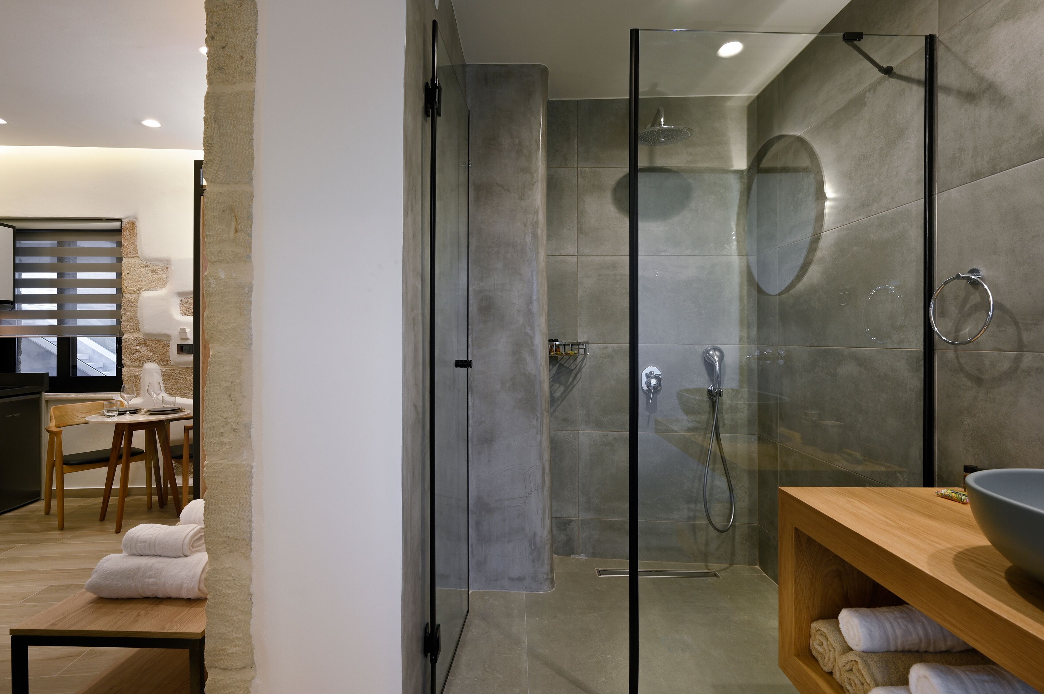 A modern bathroom with a glass-enclosed shower, a wooden vanity with a bowl sink, and neatly folded towels on a bench.
