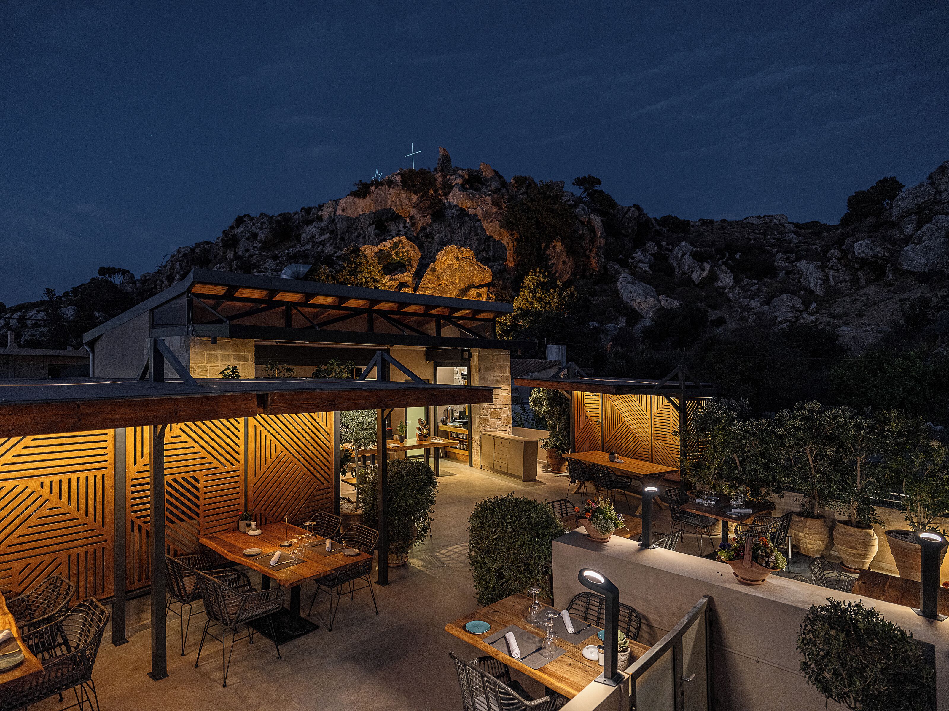 Un área de comedor al aire libre moderna con mobiliario de madera y plantas en macetas, con montañas de fondo.