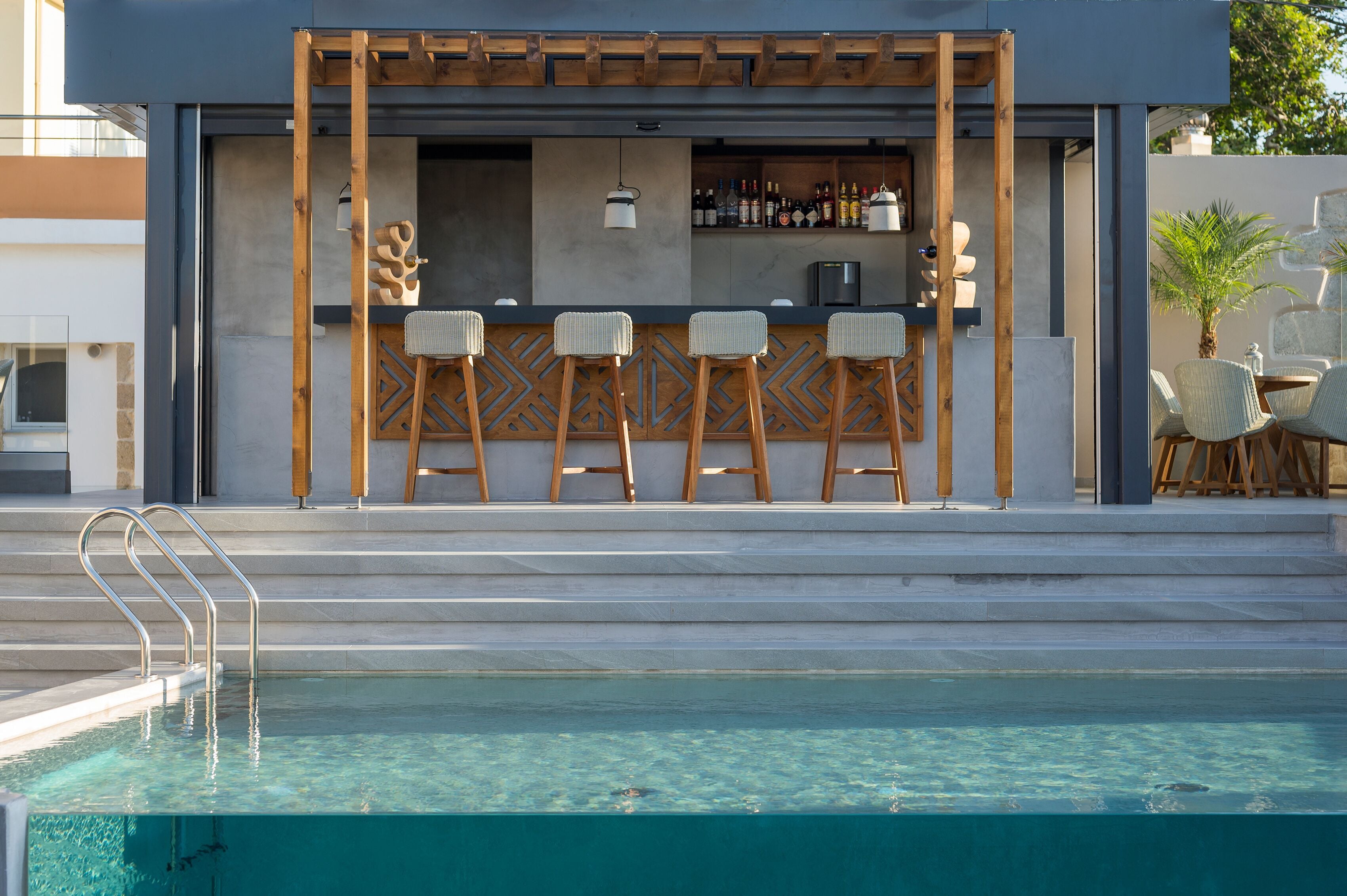 Eine Poolbar mit modernem Design, darunter eine Holzpergola, Barhocker und eine Sitzecke mit Stühlen.