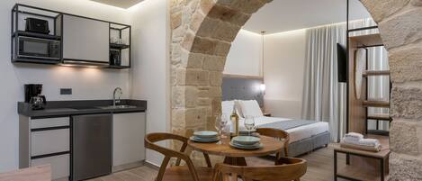 A modern kitchen with a stone archway, a dining area with wooden chairs, a bed with a view, and a small table with towels.