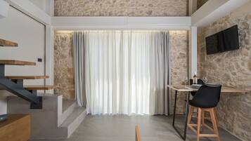 Un interior moderno con una escalera, un comedor con mesa y sillas, y un televisor montado en una pared de piedra.