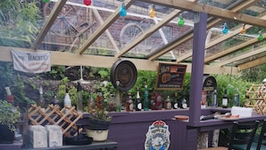 A covered outdoor bar area with a wooden structure, various bottles, and a sign indicating a whisky brand. - Stop at The Cross (Dalsjöfors)