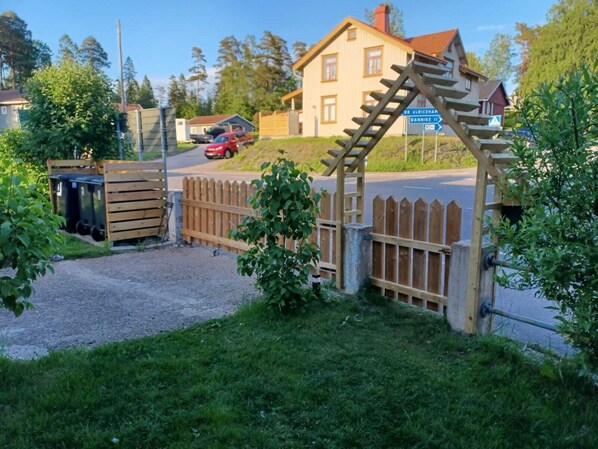 Une maison de campagne avec un portail en bois et une voiture rouge garée dans l’allée.