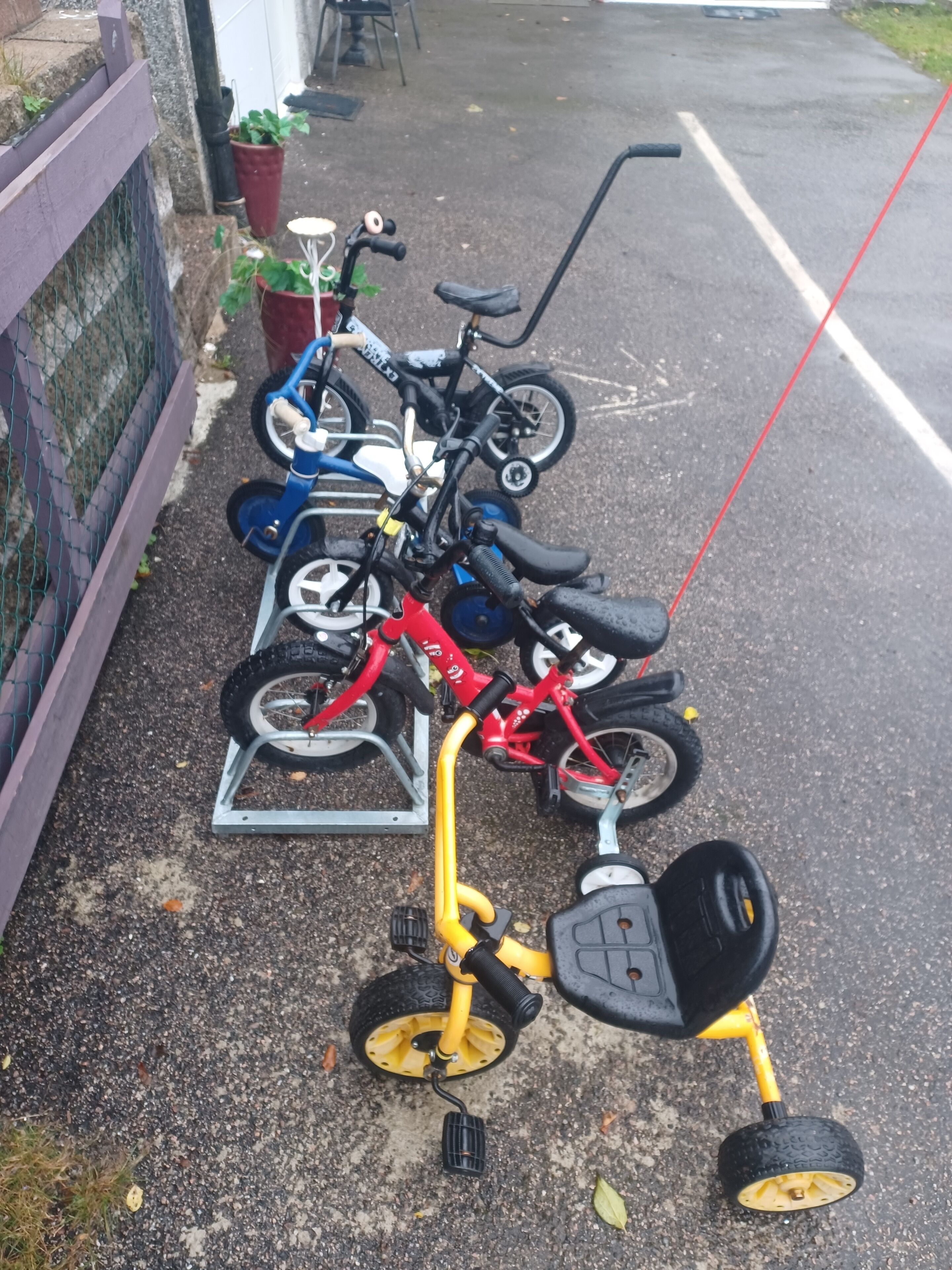 A row of children's tricycles and a small yellow tricycle with training wheels parked on a paved surface.