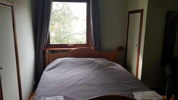 A small, cozy bedroom with a single bed, a window with curtains, and a mirror on the wall.