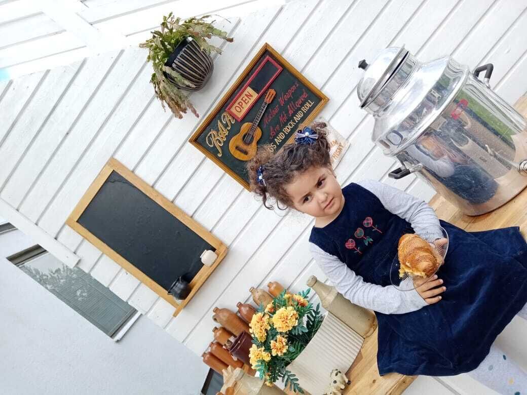 Et barn holder en sandwich i et rum med en tavle, møbler af træ og en potteplante.