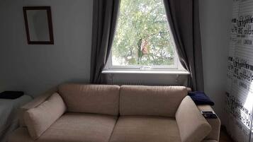 A living room with a beige sofa, a window with curtains, and a wall with printed text.