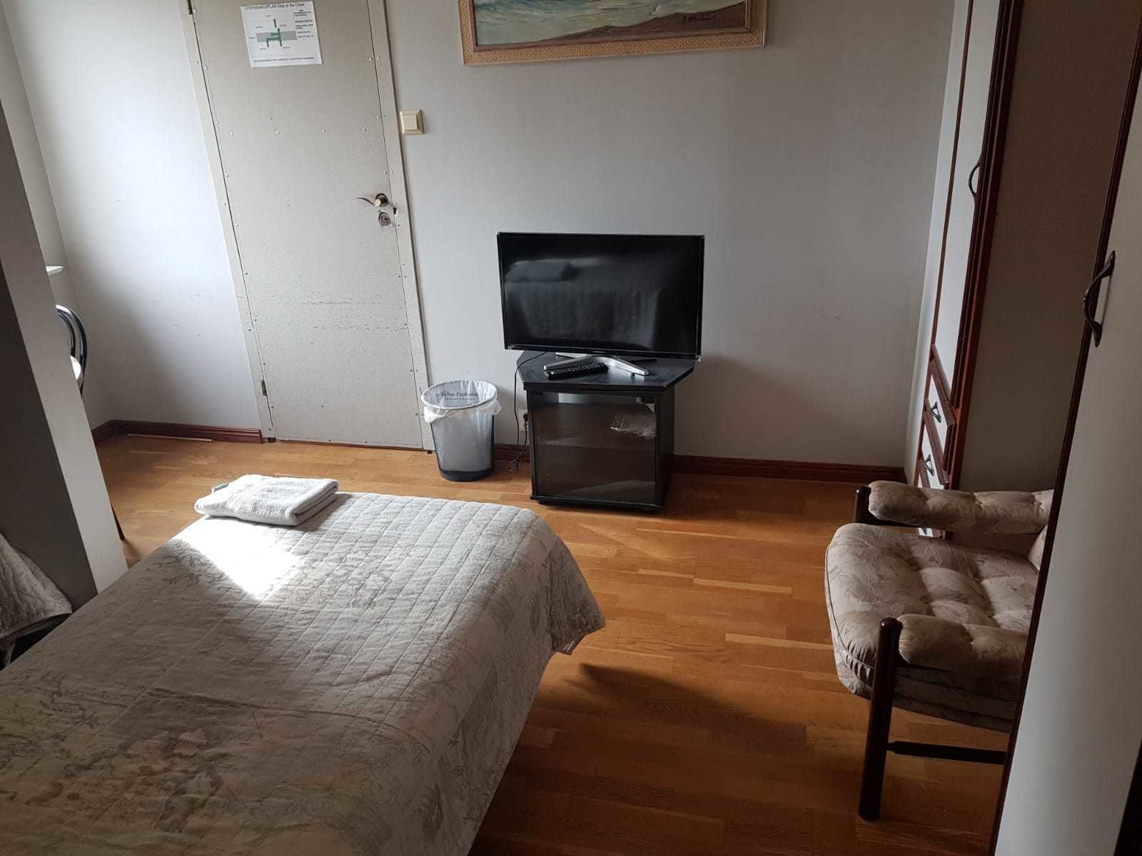 Una habitación con una cama, una silla, un televisor y un cubo de basura.