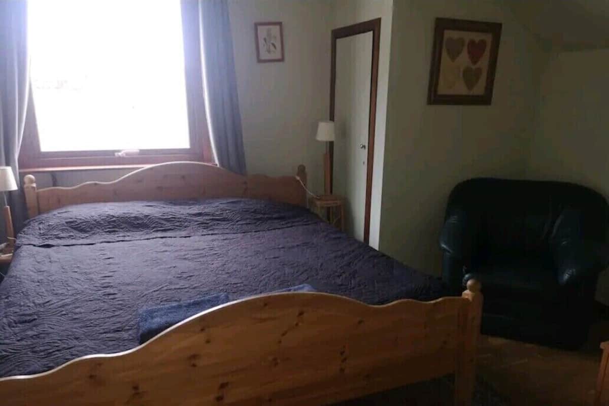A bedroom with a wooden bed, a chair, a lamp, and a door.