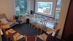 A conference room with a projector screen, a sofa, and several chairs arranged around a table. - Stop at The Cross (Dalsjöfors)