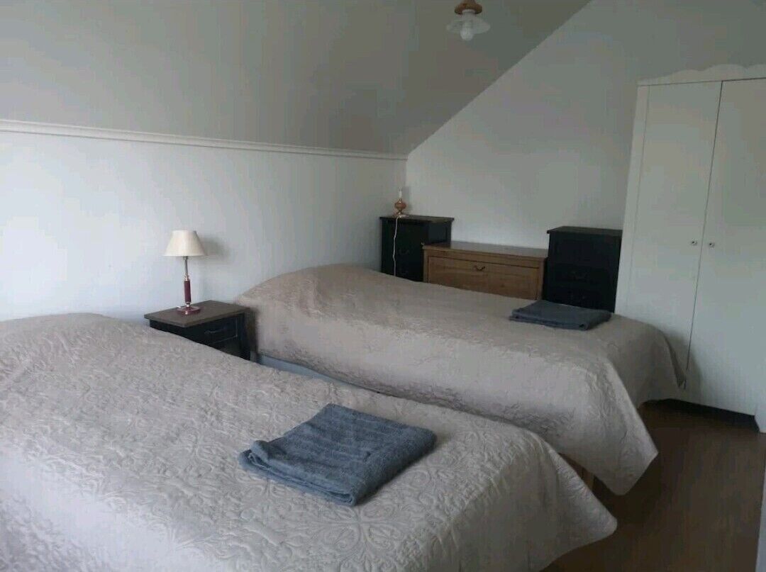 A room with two beds, a nightstand with a lamp, a dresser, and a wardrobe.