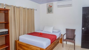 A bedroom with a wooden bed, a red blanket, a wicker chair, a shelf with baskets, and a wall-mounted air conditioner.