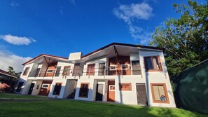 A multi-story residential building with a flat roof, multiple balconies, and a well-maintained lawn. - Hotel Vive Uvita (Bahía Ballena)