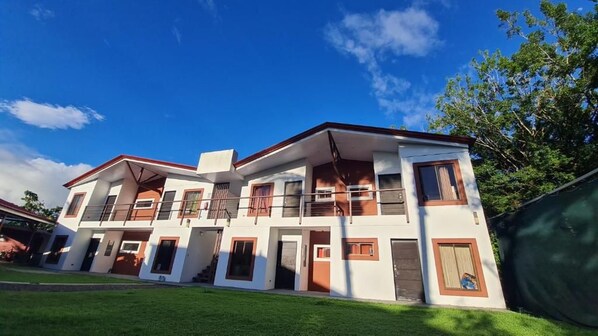A multi-story residential building with a flat roof, multiple balconies, and a well-maintained lawn.