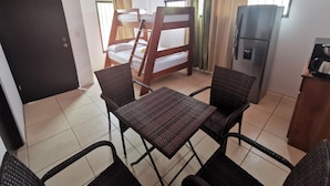 A room with a bunk bed, a refrigerator, a dining table with chairs, and a door.