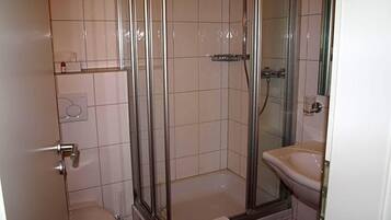 A bathroom with a glass-enclosed shower, a toilet, and a sink.