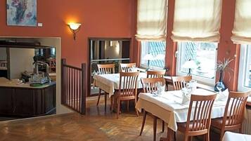 A dining area with wooden flooring, a chandelier, and large windows with curtains.