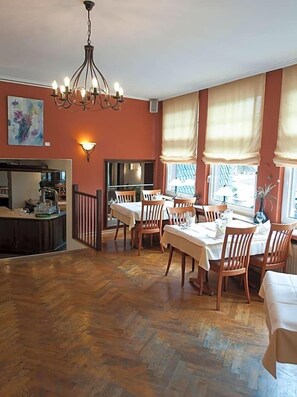 A dining area with wooden flooring, a chandelier, and large windows with curtains.