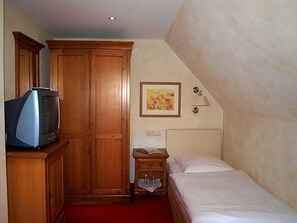 A hotel room with a bed, a wooden wardrobe, a television, a nightstand, a framed picture on the wall, and a red carpet.