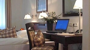 A hotel room with a bed, a desk with a laptop, a chair, a desk lamp, a potted plant, and a mirror. - Wegermann S Bio Landhaus Im Wodantal (Hattingen)