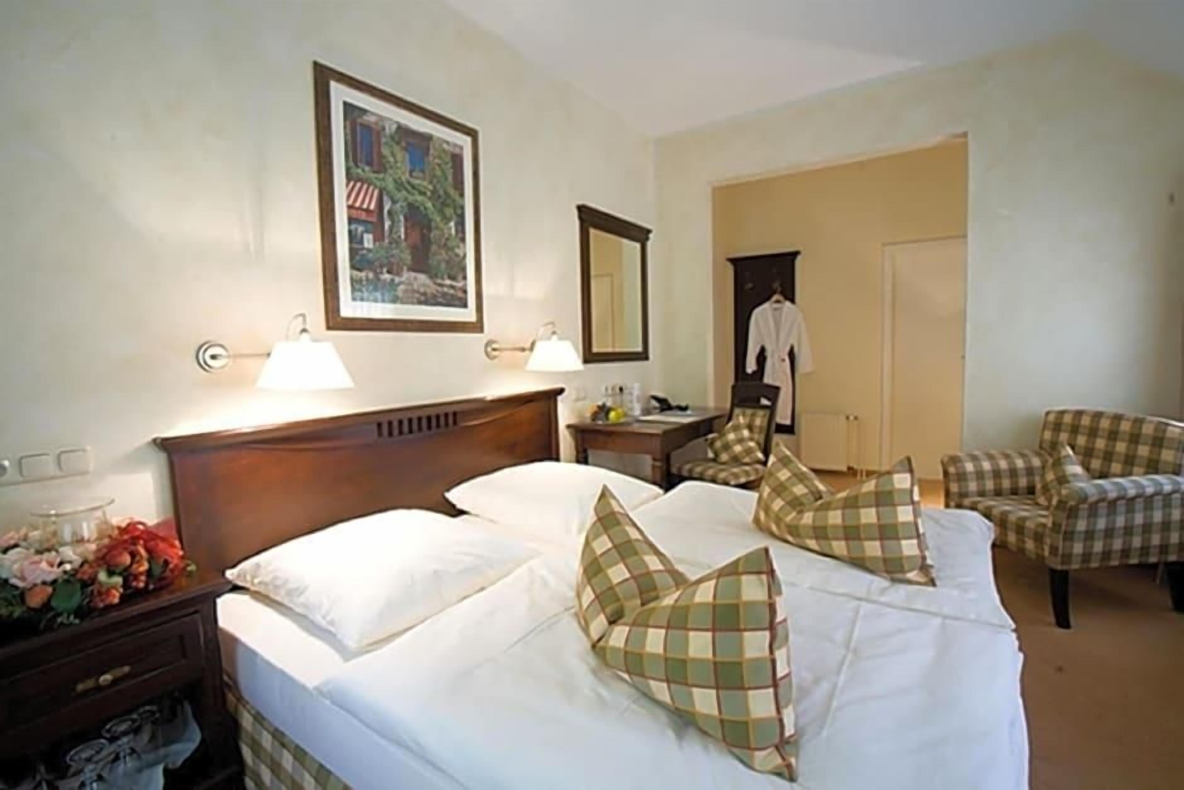A hotel room with two beds, a nightstand, a lamp, a mirror, a chair, and a coat rack.
