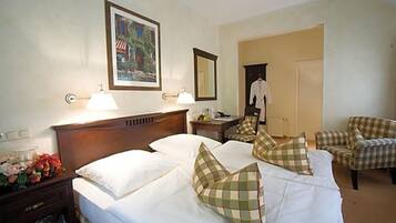 A hotel room with two beds, a nightstand, a lamp, a mirror, a chair, and a coat rack.