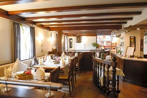 A restaurant with wooden beams, tables set for dining, and a bar area.