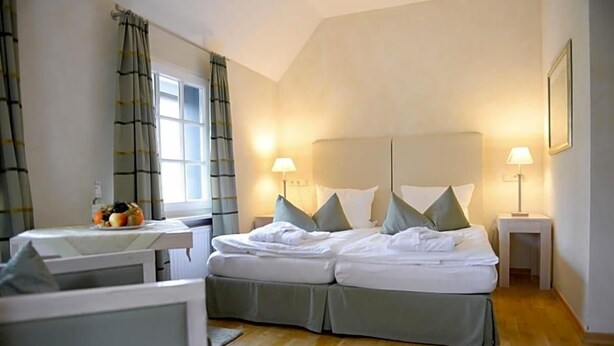 A hotel room with a bed, two bedside lamps, a window with curtains, a small table with a fruit bowl, and a framed picture on the wall. - Wegermann S Bio Landhaus Im Wodantal (Hattingen)
