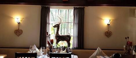 A dining area with a table set for two, a decorative deer sculpture, and heart-shaped wall decorations.