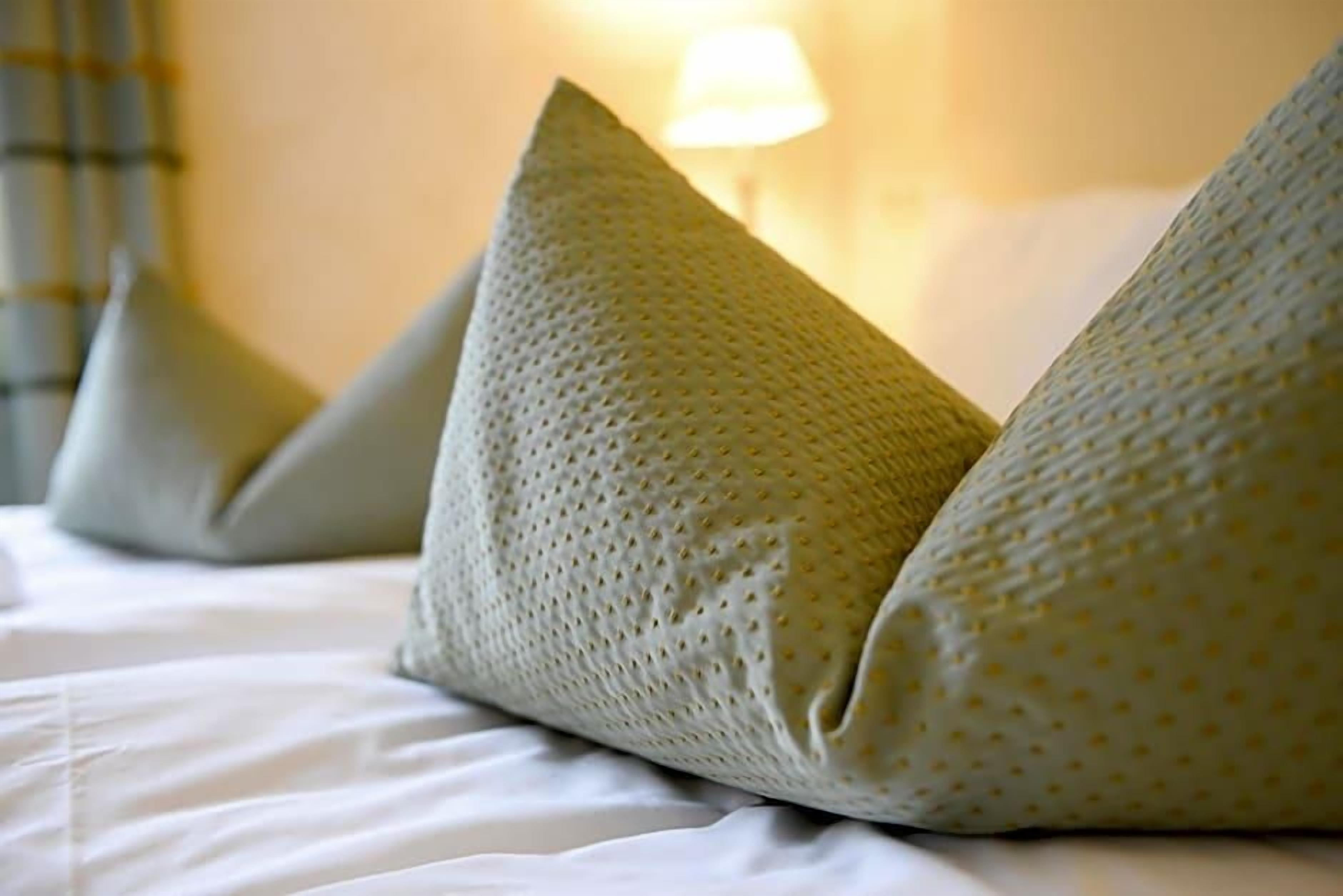 A bed with pillows and a lamp in the background.