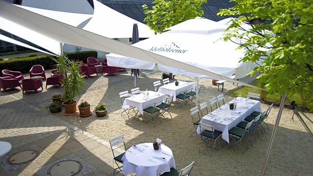 Een buitenterras met ronde tafels, stoelen en parasols, met een witte tafelkleed en een bord waarop 'Classic' staat.
