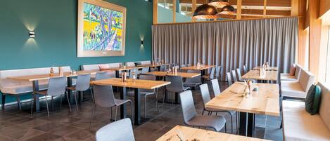 A modern dining area with multiple tables and chairs, a large abstract painting on the wall, and a view of the outdoors through large windows.