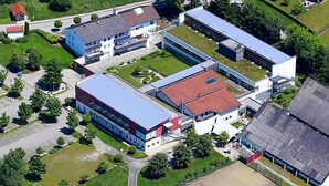 Luchtbeeld van een campus met meerdere gebouwen, groene ruimtes en een parkeerterrein.