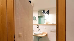 Een badkamer met witte betegelde wanden, een houten deur, een witte wastafel met een spiegel erboven en een toilet.