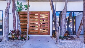 A modern building with a wooden gate, surrounded by trees and gravel. - Mi Tulum (Tulum)