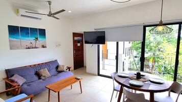 A modern living room with a sofa, a coffee table, and a dining area with chairs and a table set for two.