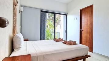 A bedroom with a bed, a ceiling fan, a window with curtains, and a wooden door.