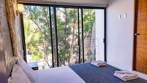 A hotel room with a bed, a window with a view of trees, and a wooden door. - Mi Tulum (Tulum)