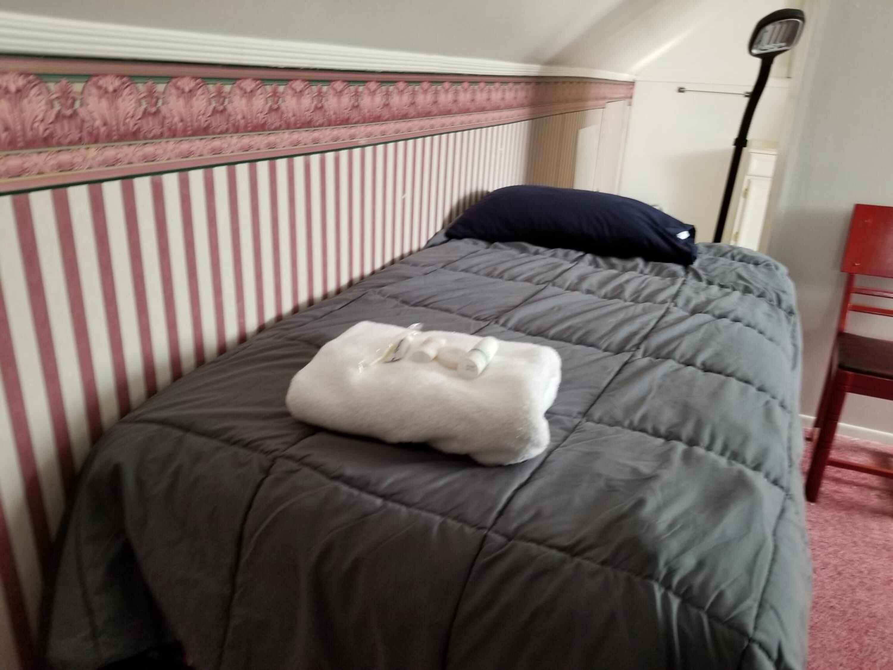 A bed with a grey quilt and a white towel on it.