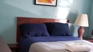Una cama bien hecha con colcha azul y beige, cabecera de madera y mesita de noche con lámpara.